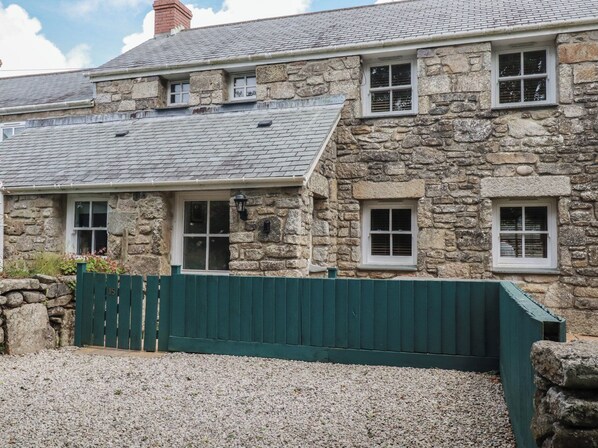 A stone building with multiple windows, a green fence, and a gravel driveway.