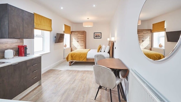 A modern hotel room with a bed, a dining area, a kitchen, and a large mirror. - Host & Stay | Studio Pod 2 (Saltburn-by-the-Sea)