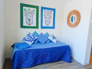A bedroom with a bed, blue bedding, and two framed artworks on the wall.