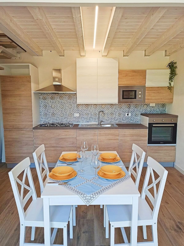 A modern kitchen with wooden cabinets, a central island, and a dining table set for four with white chairs.