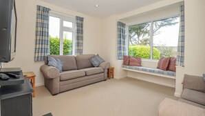 A living room with a sofa, a television, and a window seat with curtains. - Hillcroft Bungalow (Wadebridge)