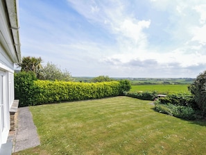 A well-maintained lawn with a hedge, a stone pathway, and a view of a green field and distant landscape.