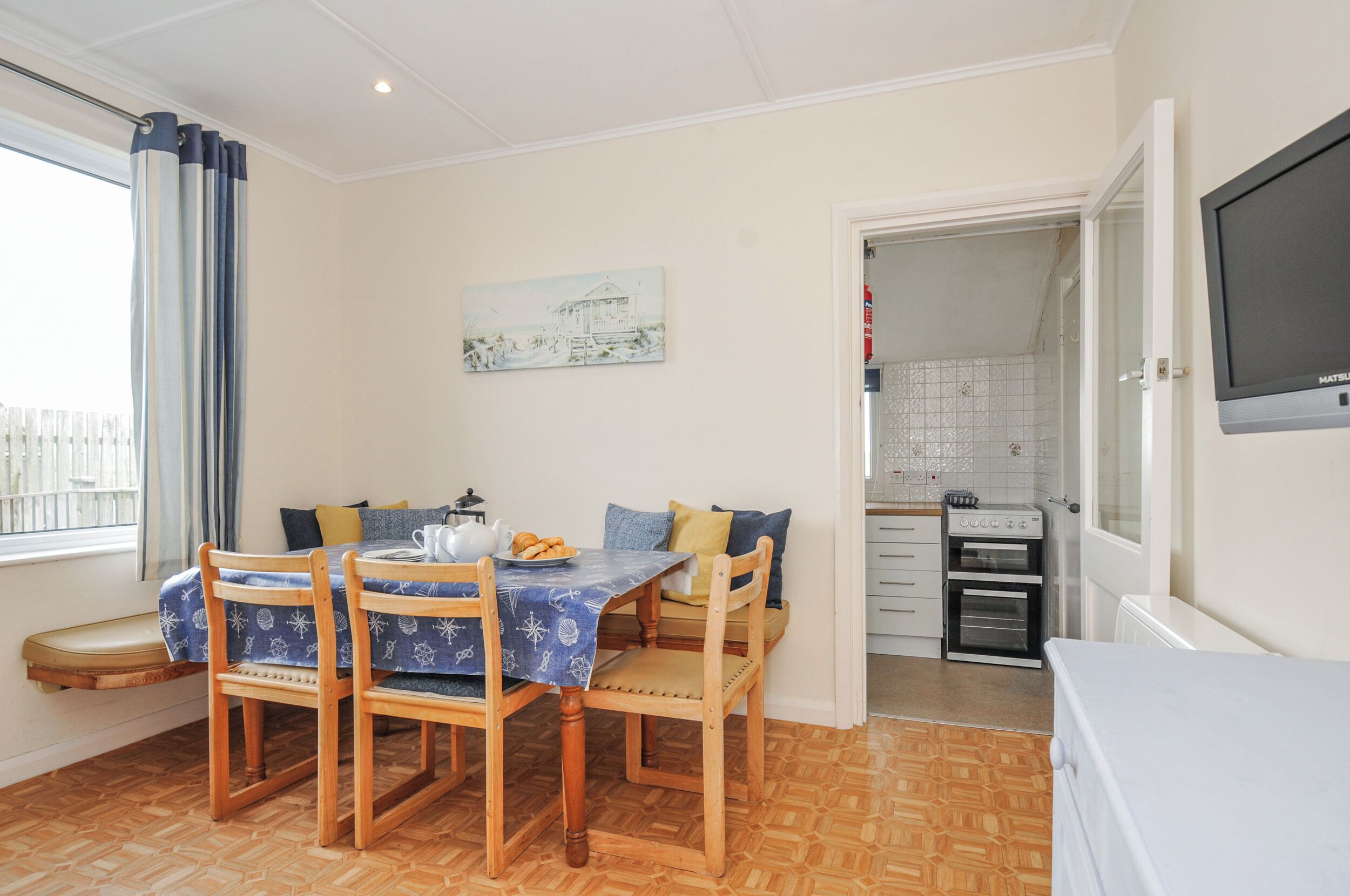 A dining area with a table, chairs, and a bench. There is a kitchen with appliances and a television.