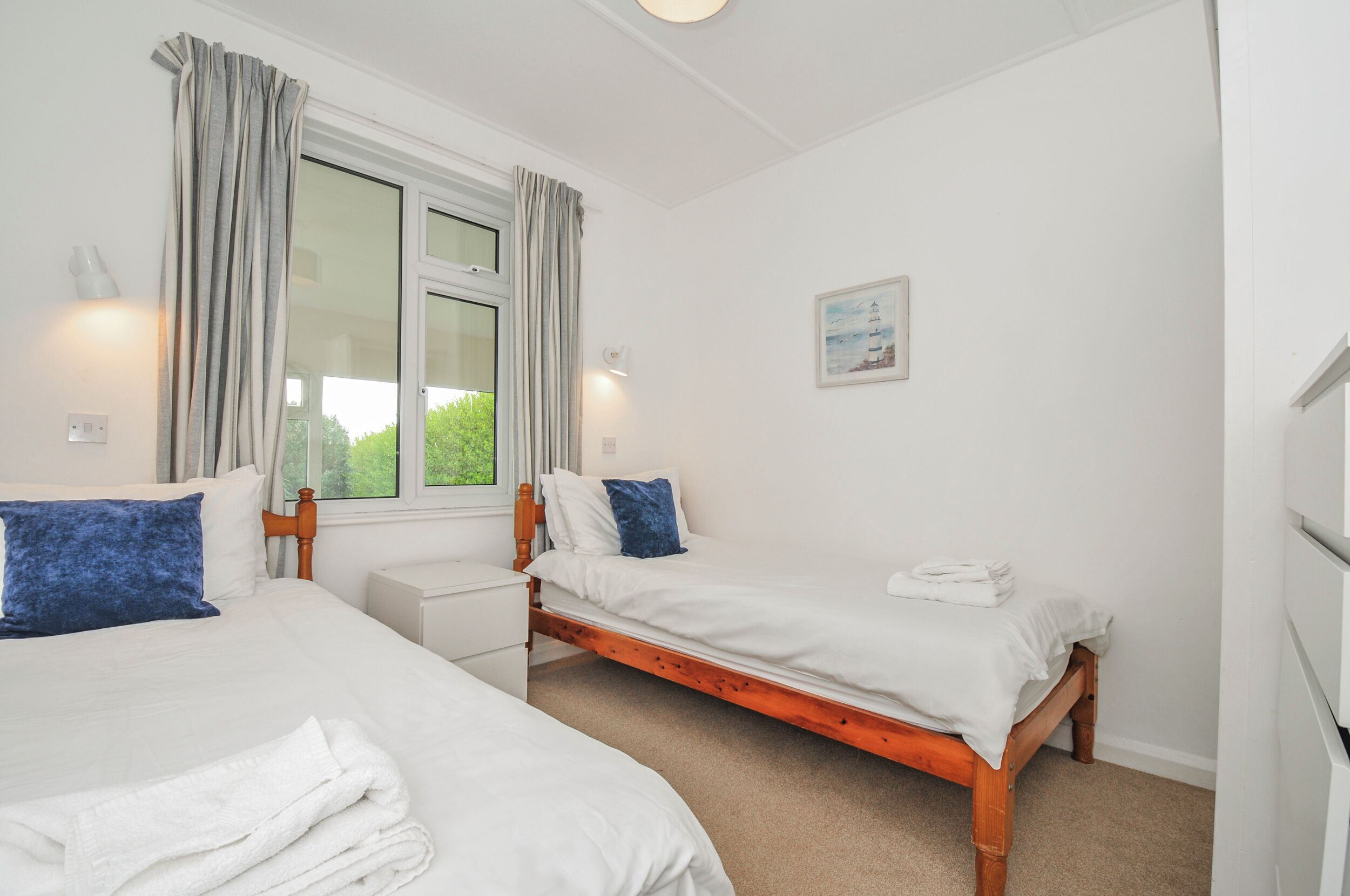 Une chambre avec deux lits, une fenêtre avec des rideaux, une table de chevet et une lampe fixée au mur.