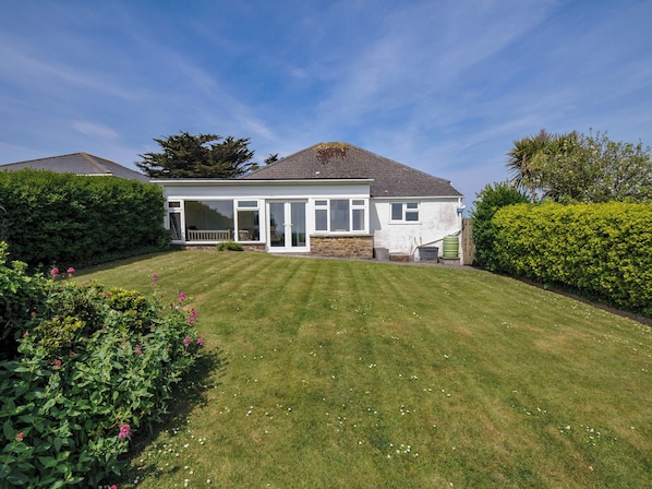 A two-story house with a large lawn, a conservatory, and a stone wall.