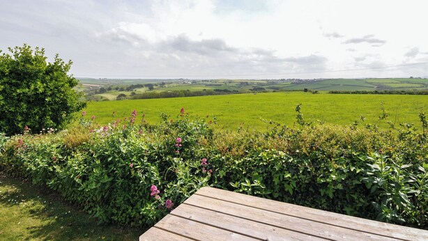 A wooden deck overlooking a green field with a distant view of rolling hills. - Hillcroft Bungalow (Wadebridge)