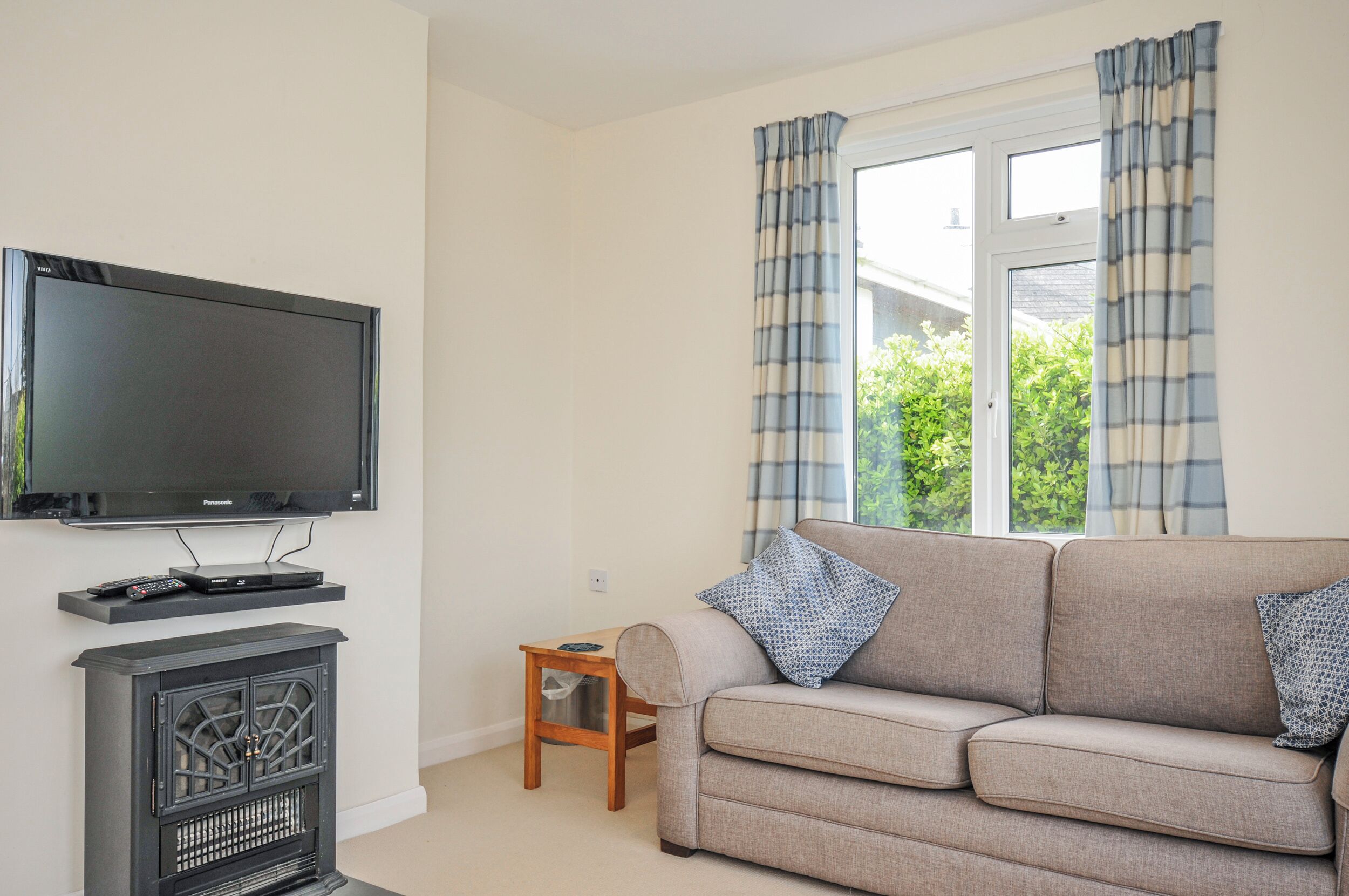 A living room with a flat-screen TV, a fireplace, a sofa, and a window with curtains.