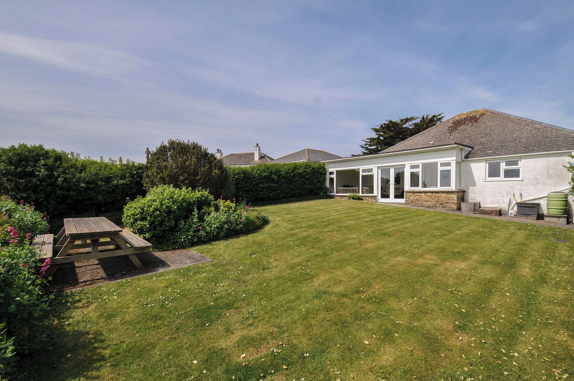 A residential property with a well-maintained lawn, a wooden picnic table, and a house with a large windowed porch.