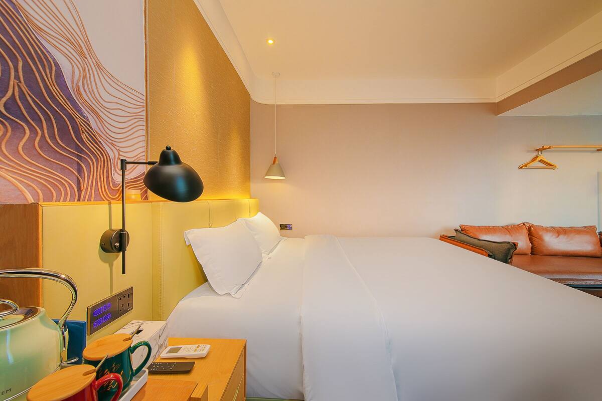 A hotel room with a bed, bedside table, lamp, and a wall with a decorative pattern.