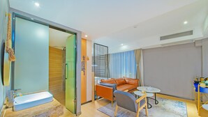 Una habitación de hotel moderna con ducha de vidrio, un sofá, una mesita pequeña y una alfombra azul.