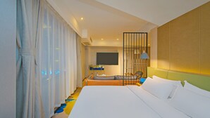 Habitación de hotel con una cama grande, un escritorio con silla, televisor montado en la pared y ventana con cortinas.