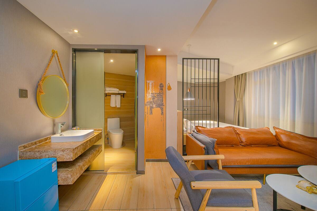 A modern hotel room with a bathroom, a sofa, and a dining table.