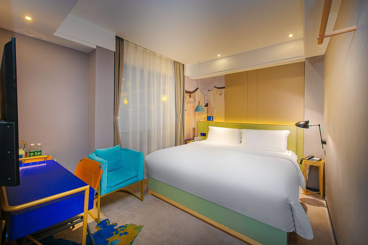 A hotel room with a bed, a desk, a chair, a TV, and a nightstand.