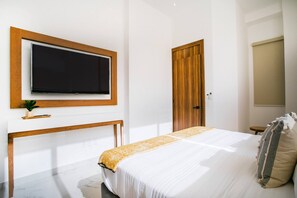 A bedroom with a bed, a TV mounted on the wall, a wooden door, and a bedside table with a plant.
