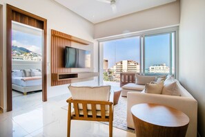 A modern living room with a flat-screen TV, a sofa, a chair, and a coffee table. - NEW Bright & Airy 2bdrm @ D'esire | Pool, Gym (Puerto Vallarta)