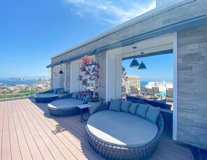 A rooftop terrace with a view of the city, featuring a seating area with cushions and planters. - NEW Bright & Airy 2bdrm @ D'esire | Pool, Gym (Puerto Vallarta)