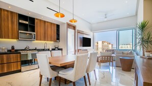 Una cocina moderna con armarios de madera, un microondas integrado y un comedor con piso de mármol y sillas blancas.