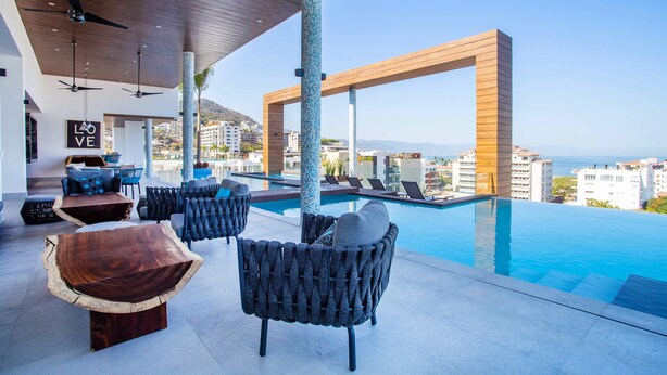 Una piscina infinita en la azotea con mobiliario moderno, techo de madera y vistas a la ciudad.