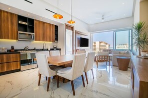 A modern kitchen with wooden cabinets, a dining area with a marble floor, and a large window offering a city view.