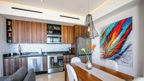 A modern kitchen with wooden cabinets, stainless steel appliances, and a dining area with a wooden table and chairs. - Luxury D’esire 1BR w/ City View & Private BBQ (Puerto Vallarta)