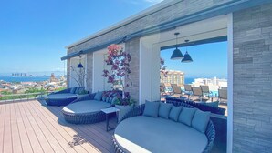 A rooftop terrace with two round seating areas, a view of the city and ocean, and a stone wall. - Luxury D’esire 1BR w/ City View & Private BBQ (Puerto Vallarta)