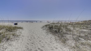 Caminho de areia que leva ao oceano, com vegetação rala em ambos os lados.