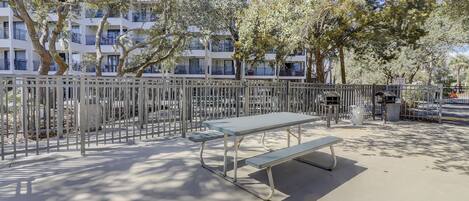 A park with a metal fence, a bench, and a trash bin.