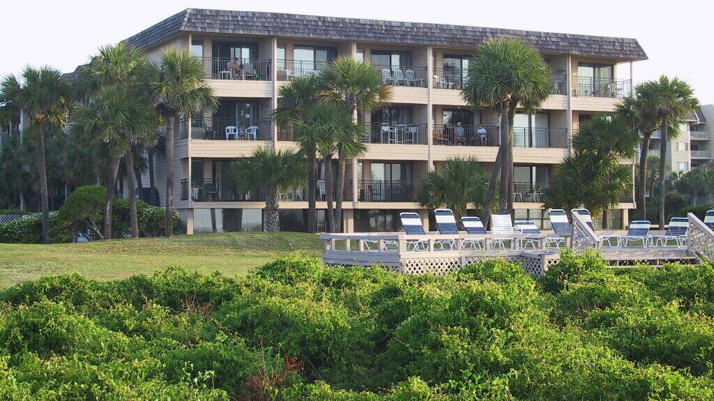 A multi-story hotel with balconies, a pool area with sun loungers, and palm trees.