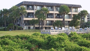 Um hotel com vários andares, varandas, área de piscina com espreguiçadeiras e palmeiras.