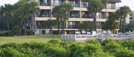 A multi-story hotel with balconies, a pool area with sun loungers, and palm trees.