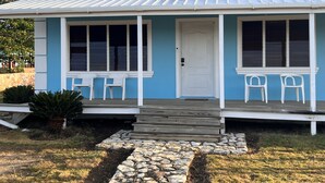 Een huis met een blauwe gevel, een witte deur en een veranda met twee witte stoelen.