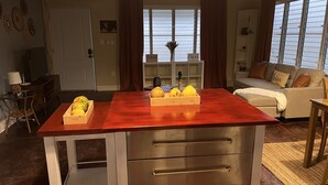 Een woonkamer met een houten tafel, een bank en een televisie. Op de muren staan decoratieve objecten en er is een raam met gordijnen.
