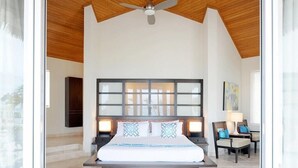 A modern hotel room with a large bed, a ceiling fan, and a view through a glass door.