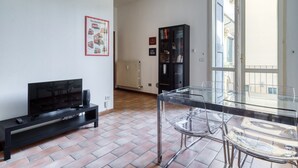 Ein modernes Wohnzimmer mit Fernseher, schwarzem Unterhaltungsschrank und einem Glastisch mit Stühlen.