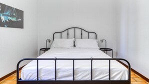 Ein Einzelbett mit Metallgestell, weißer Bettwäsche und zwei Nachttischen.