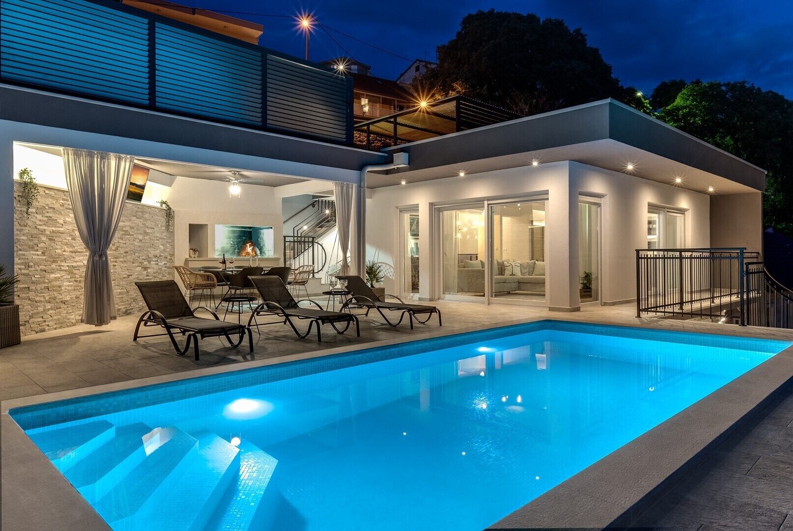 A modern house with a swimming pool, outdoor seating, and a staircase leading to a balcony.