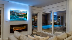 Een moderne woonkamer met een open haard, een grote flatscreen-tv en uitzicht op een buitenzwembad.