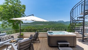 Een dakterras met een jacuzzi, een zithoek en een prachtig uitzicht op de bergen.