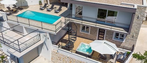 Et moderne hus med to etager, en pool på taget og en udendørs spa samt udendørs møbler.