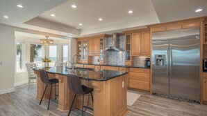 A spacious kitchen with wooden cabinets, a stainless steel refrigerator, and a large island with bar stools. - 29 Turtle Lane Club: BESTNEST by Beverly Serral OCEANFRONT (Hilton Head Island)
