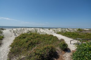 A sandy beach path with vegetation and a clear sky.