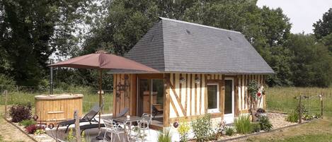 Una pequeña cabaña de madera con techo inclinado, un patio con mobiliario exterior y un jacuzzi.