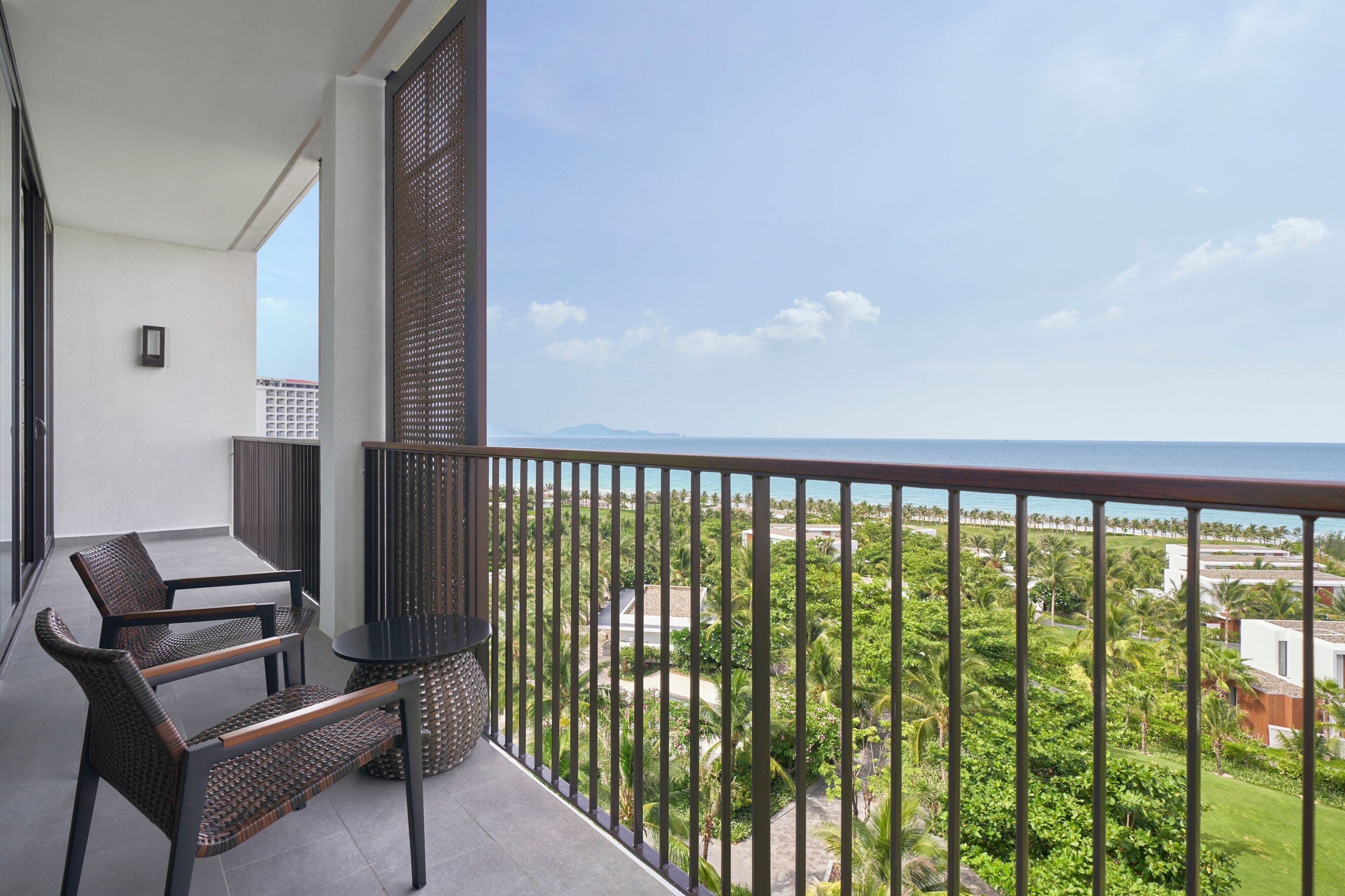 A balcony with a view of the sea, a table, and two chairs.