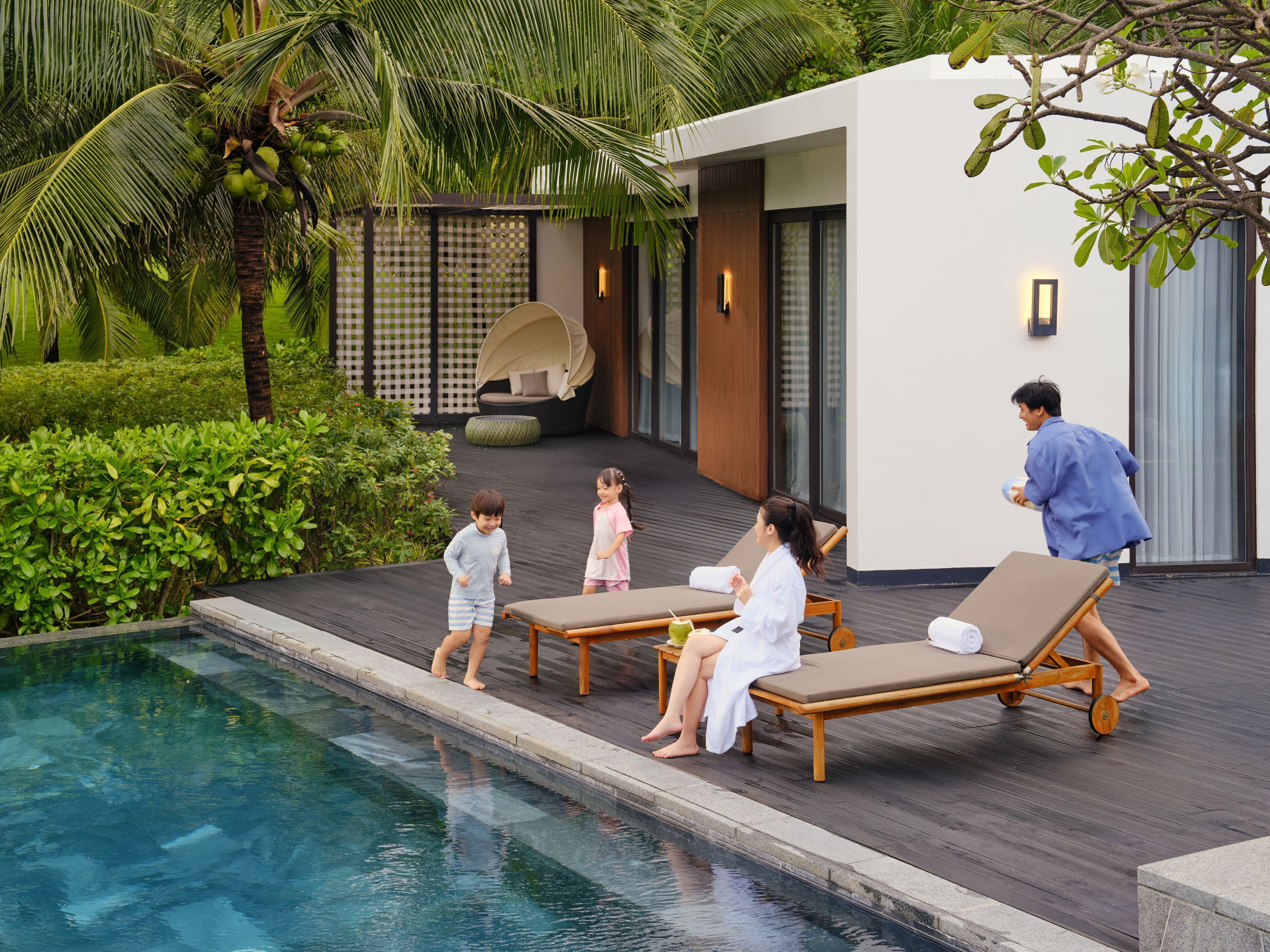 A poolside area with lounge chairs, a pool, and a modern building with a checkered fence and a hanging chair.