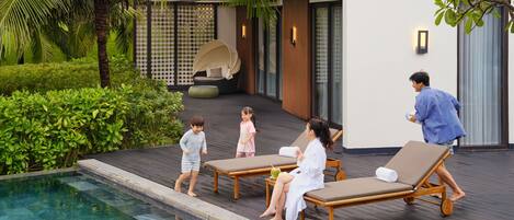 A poolside area with lounge chairs, a pool, and a modern building with a checkered fence and a hanging chair.