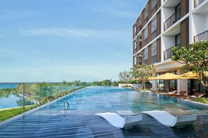 A modern hotel with a rooftop infinity pool overlooking the ocean, surrounded by palm trees and lounge chairs. - The Westin Resort & Spa Cam Ranh (Cam Lam)