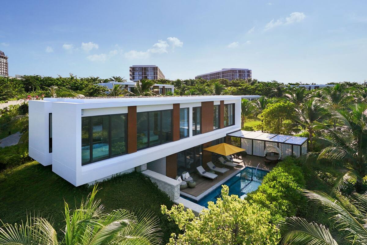 A modern house with a pool, surrounded by lush greenery and palm trees.
