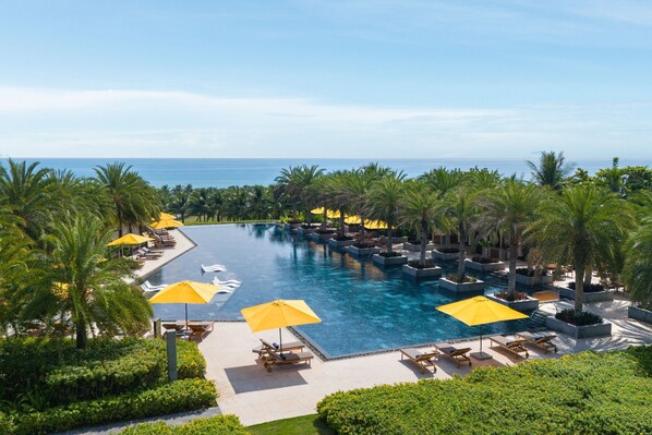 A large infinity pool with yellow umbrellas, surrounded by palm trees and lounge chairs, overlooking the ocean. - The Westin Resort & Spa Cam Ranh (Cam Lam)
