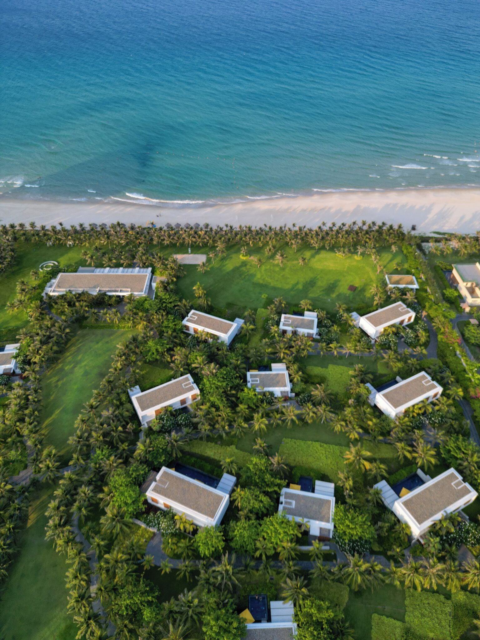 Luchtbeeld van een resort met meerdere villa's, een strand en een golfbaan.