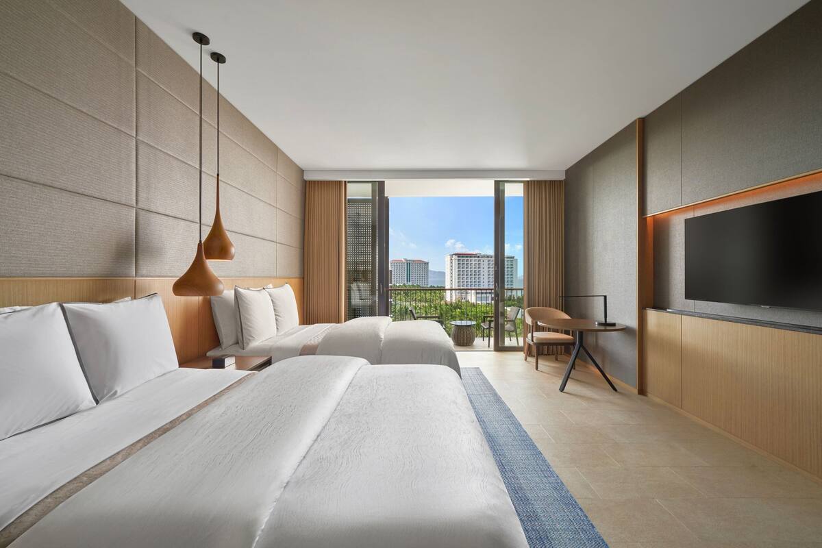 A modern hotel room with two beds, a TV, and a balcony with a city view.